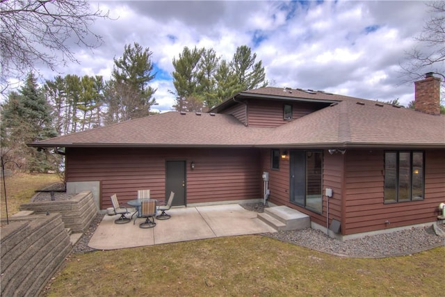 rear view of property with a shingled roof, a patio, a chimney, and a lawn