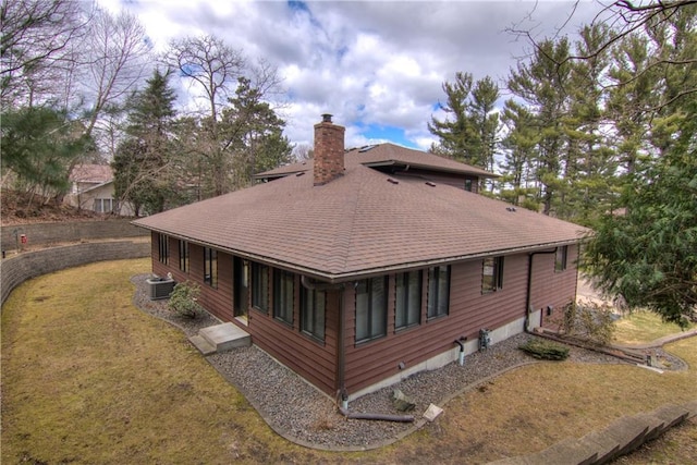 rear view of house featuring a chimney, a yard, central AC unit, and a shingled roof