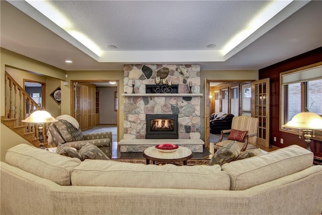 living area featuring a tray ceiling, stairs, and a stone fireplace