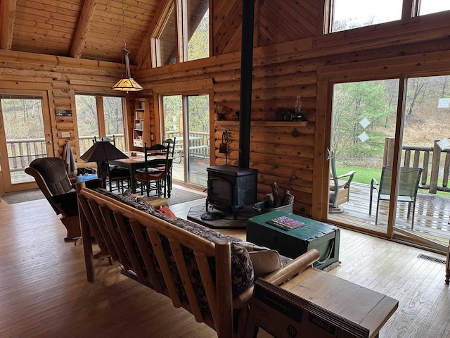 living area with beamed ceiling, a wood stove, wood-type flooring, and plenty of natural light