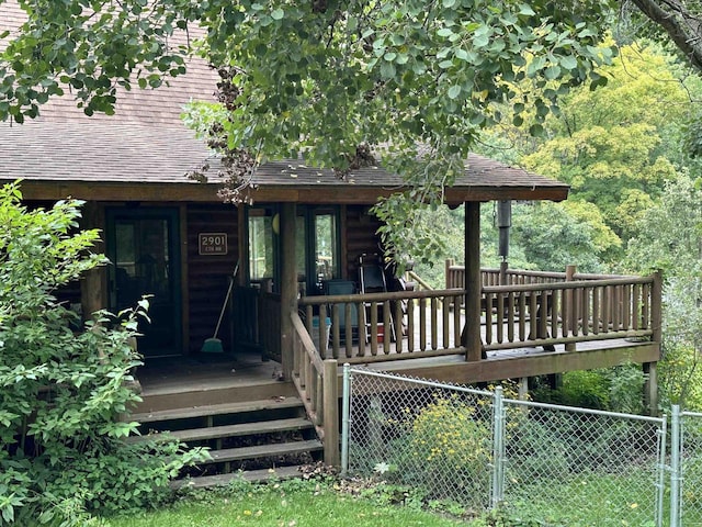 entrance to property featuring a porch, roof with shingles, and fence