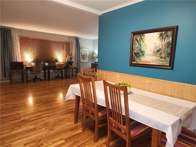 dining area featuring wood walls, wood finished floors, wainscoting, and ornamental molding