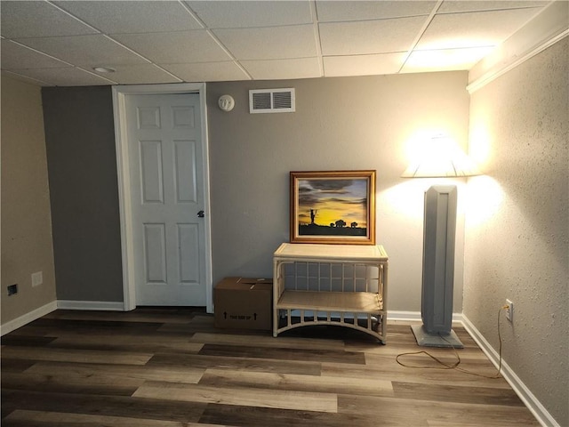 living area with a drop ceiling, visible vents, wood finished floors, and baseboards