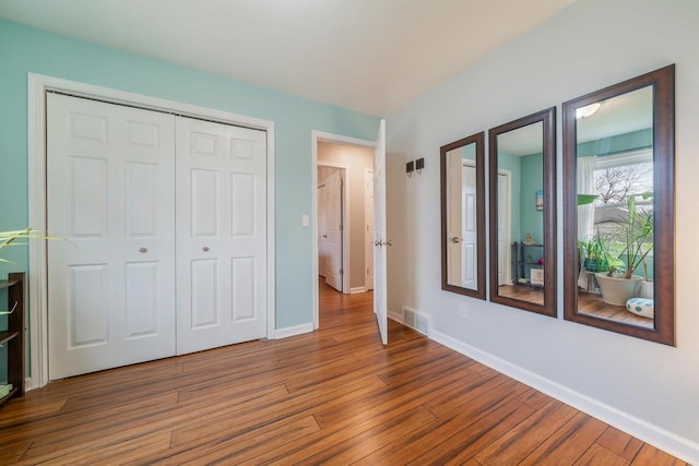unfurnished bedroom with baseboards, a closet, visible vents, and wood finished floors
