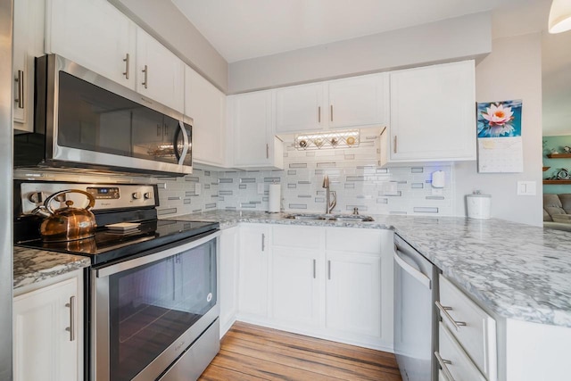 kitchen with a sink, light stone counters, backsplash, white cabinetry, and appliances with stainless steel finishes