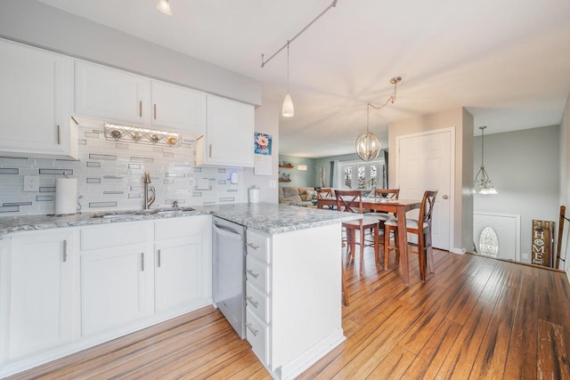 kitchen with a peninsula, light wood finished floors, a sink, stainless steel dishwasher, and backsplash