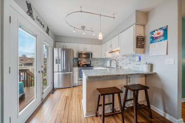 kitchen with a sink, a peninsula, light wood-style floors, stainless steel appliances, and tasteful backsplash