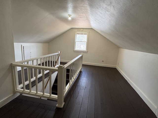 additional living space featuring baseboards, a textured ceiling, lofted ceiling, and dark wood-style floors