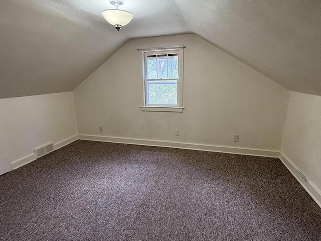 additional living space with lofted ceiling, dark colored carpet, baseboards, and visible vents