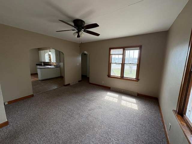 carpeted spare room with arched walkways, baseboards, and a ceiling fan