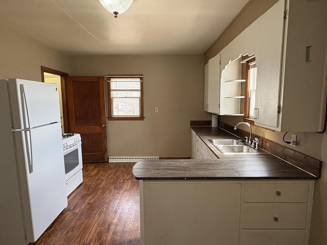 kitchen featuring a peninsula, a sink, dark countertops, white cabinetry, and white appliances