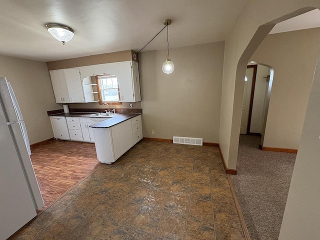kitchen featuring freestanding refrigerator, visible vents, arched walkways, dark countertops, and white cabinets