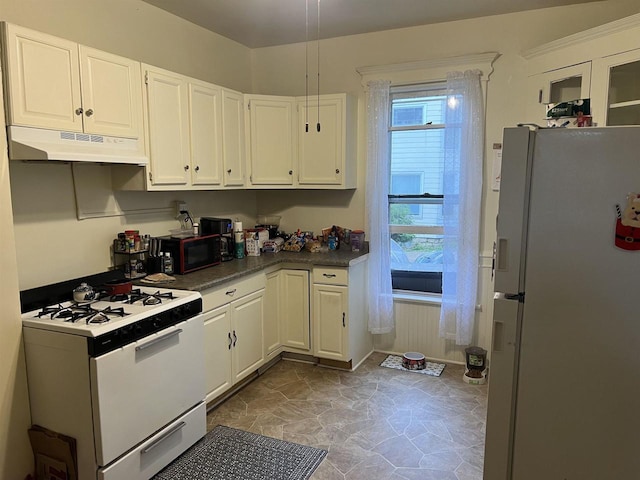 kitchen with dark countertops, stone finish floor, white cabinetry, white appliances, and under cabinet range hood
