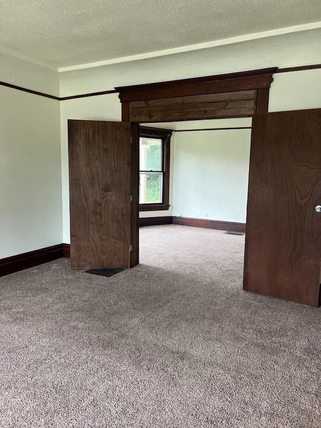 spare room with a textured ceiling, carpet flooring, and baseboards