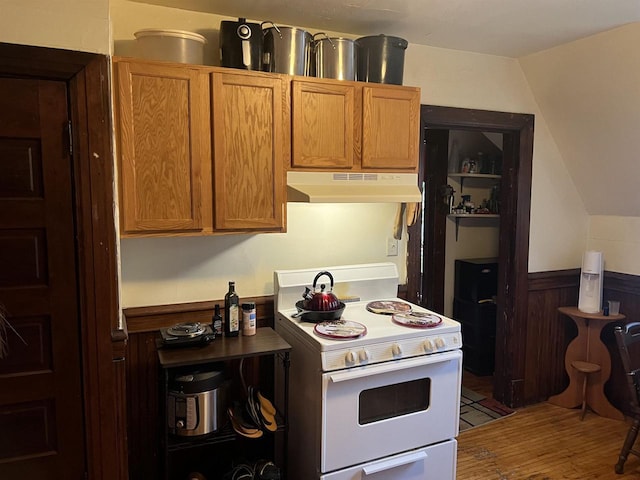 kitchen featuring brown cabinetry, wood finished floors, under cabinet range hood, white electric range oven, and wainscoting