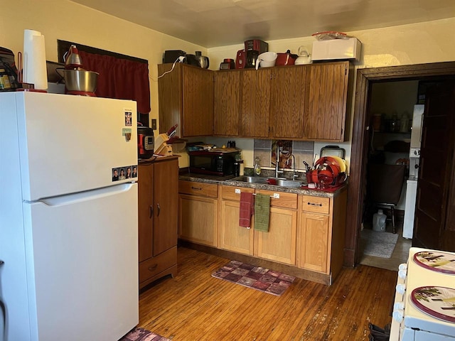 kitchen with a sink, freestanding refrigerator, black microwave, and dark wood-style floors