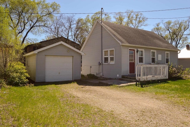 view of front facade with roof with shingles, a garage, an outbuilding, a front yard, and dirt driveway