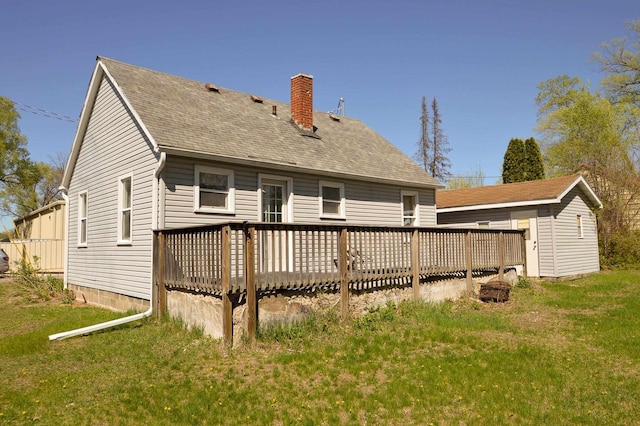 back of house featuring a chimney, a yard, an outbuilding, a deck, and roof with shingles