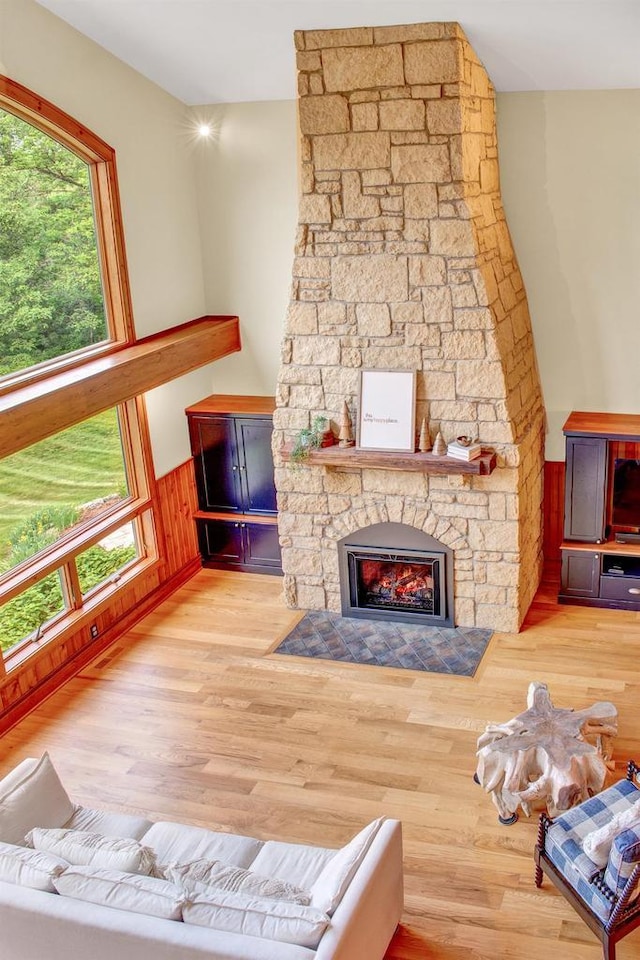 living room featuring a wainscoted wall, a stone fireplace, and wood finished floors