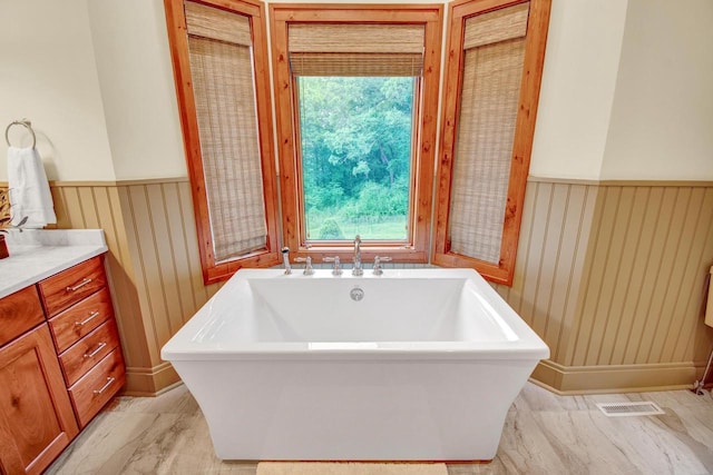 bathroom with a freestanding bath, vanity, visible vents, and wainscoting