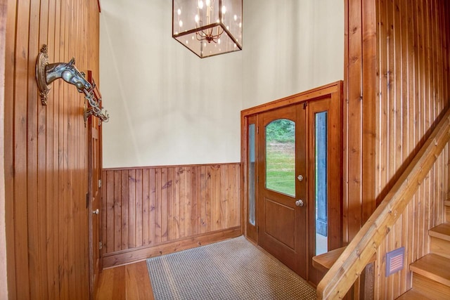 foyer featuring wood walls, a wainscoted wall, a towering ceiling, stairway, and a notable chandelier