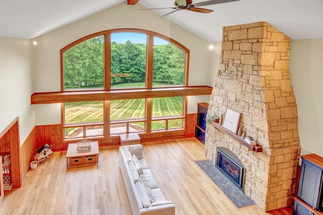 living room featuring ceiling fan, a stone fireplace, and a healthy amount of sunlight