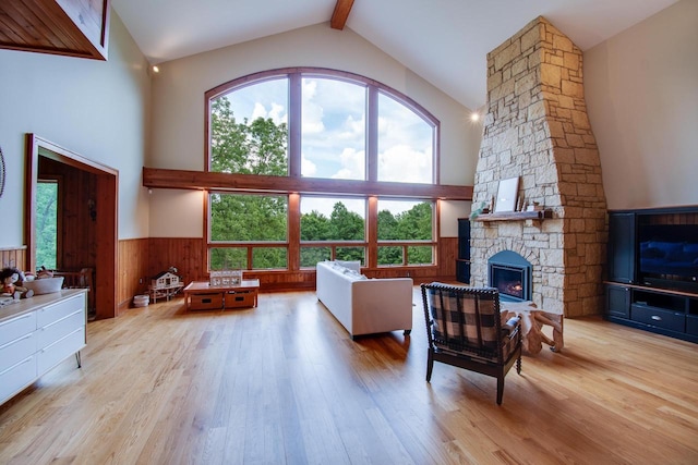 living area with a stone fireplace, high vaulted ceiling, a wainscoted wall, wood finished floors, and beamed ceiling
