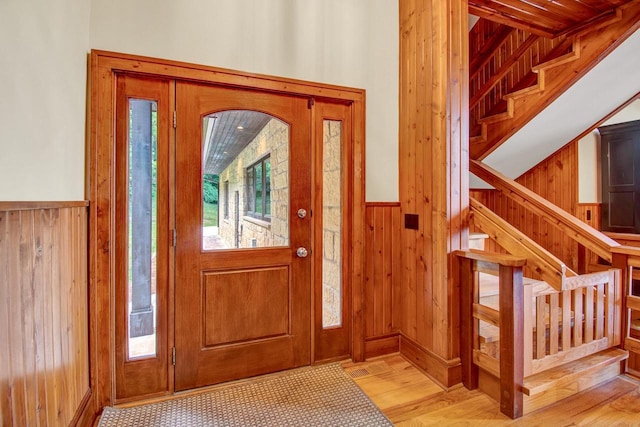 entrance foyer featuring wainscoting, stairs, wooden walls, and wood finished floors