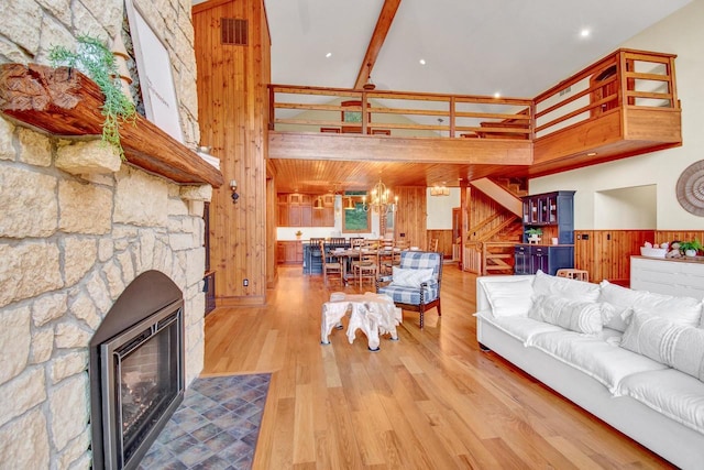 living room with a stone fireplace, visible vents, wood walls, a towering ceiling, and stairway