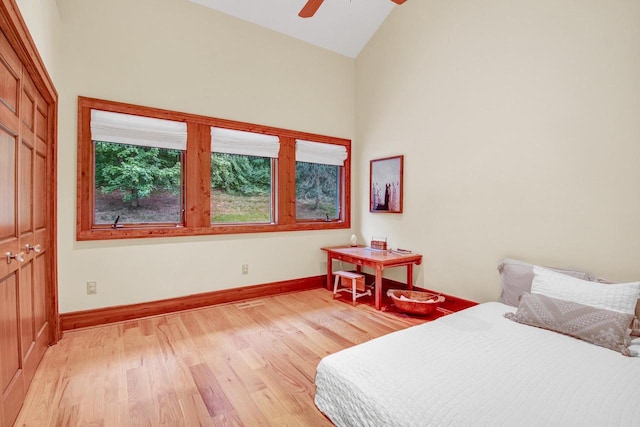bedroom featuring baseboards, light wood-type flooring, a ceiling fan, and high vaulted ceiling