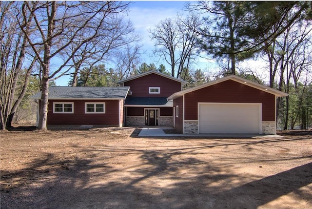 tri-level home with dirt driveway, a garage, and stone siding