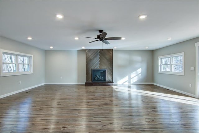 unfurnished living room featuring a large fireplace, baseboards, a ceiling fan, and wood finished floors