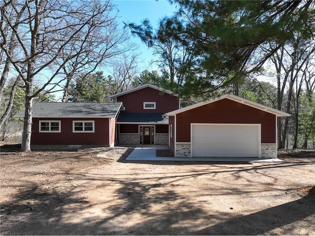 view of front of home featuring stone siding, dirt driveway, and a garage