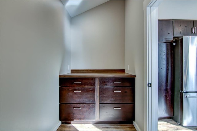 interior space featuring freestanding refrigerator, baseboards, dark brown cabinets, and wood finished floors