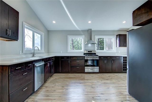kitchen featuring a sink, wall chimney range hood, appliances with stainless steel finishes, light countertops, and light wood-style floors