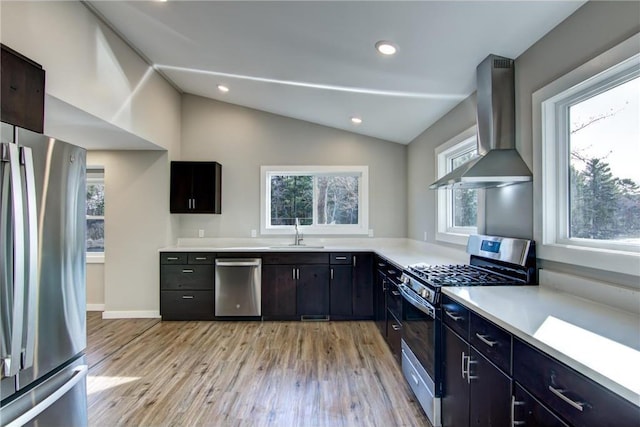 kitchen featuring a sink, light wood-type flooring, wall chimney exhaust hood, light countertops, and appliances with stainless steel finishes
