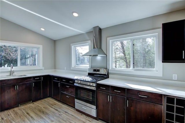 kitchen with a sink, lofted ceiling, light wood-type flooring, wall chimney exhaust hood, and gas range