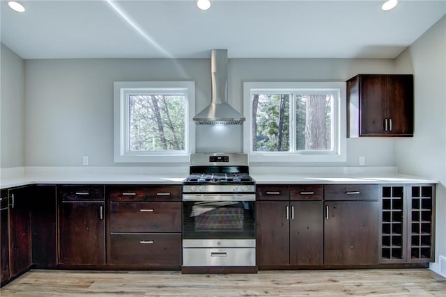 kitchen with light wood-style flooring, gas range, light countertops, and wall chimney exhaust hood