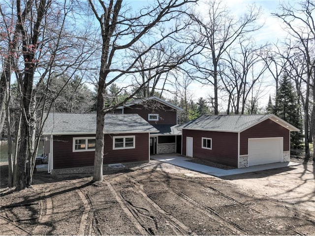 view of front facade featuring a detached garage, stone siding, and an outbuilding