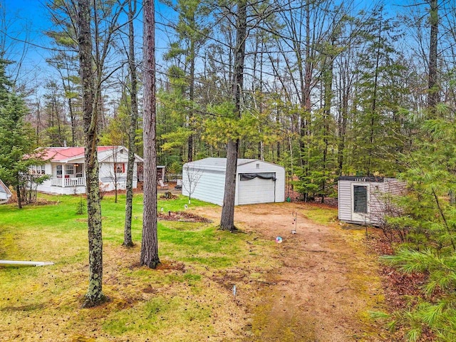 view of yard with a detached garage, dirt driveway, and an outbuilding