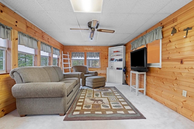 living area featuring a drop ceiling, wood walls, ceiling fan, and carpet floors