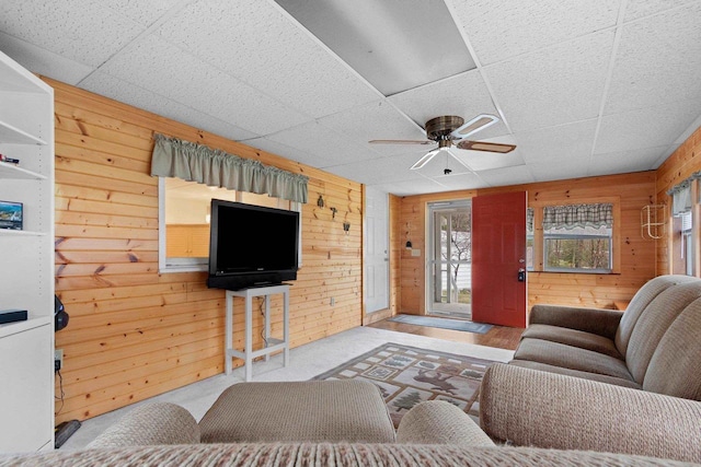 living room featuring a paneled ceiling, wooden walls, and ceiling fan