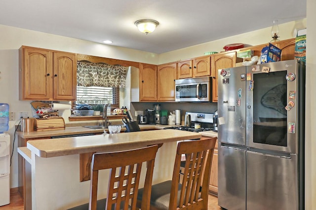 kitchen featuring a sink, stainless steel appliances, a breakfast bar, light countertops, and a kitchen island