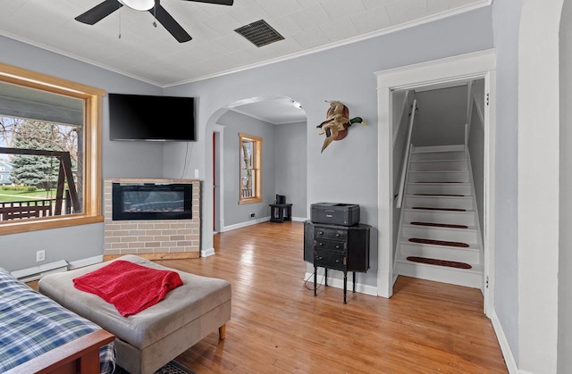 living room with light wood finished floors, crown molding, visible vents, ceiling fan, and arched walkways