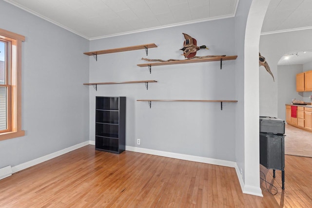 unfurnished living room featuring crown molding, light wood-type flooring, baseboards, and arched walkways