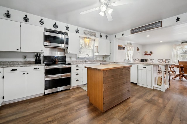 kitchen featuring stainless steel appliances, a peninsula, ceiling fan, and dark wood-type flooring