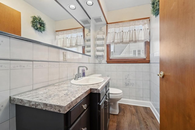 bathroom featuring tile walls, toilet, visible vents, vanity, and wood finished floors