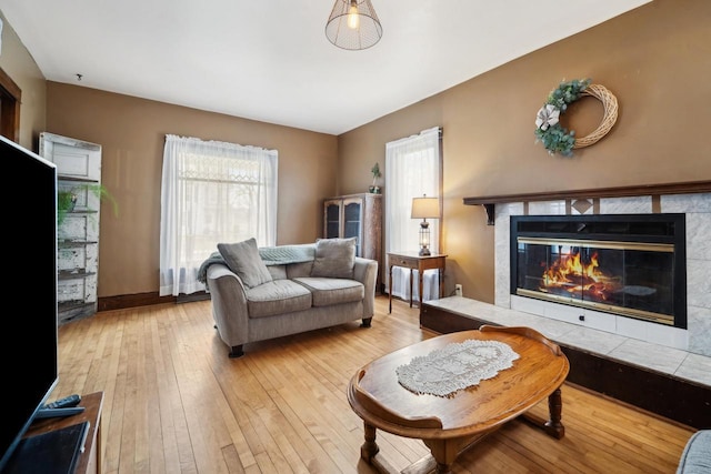 living area with baseboards, a healthy amount of sunlight, a tiled fireplace, and wood-type flooring