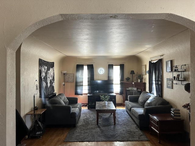 living area with arched walkways, wood finished floors, and a textured wall