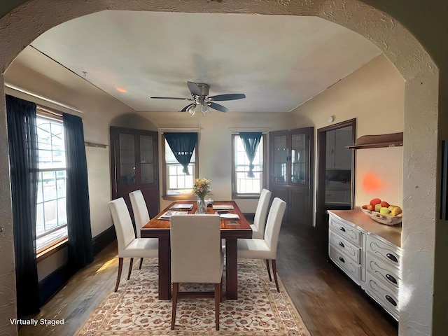 dining area featuring ceiling fan, arched walkways, and dark wood-style floors